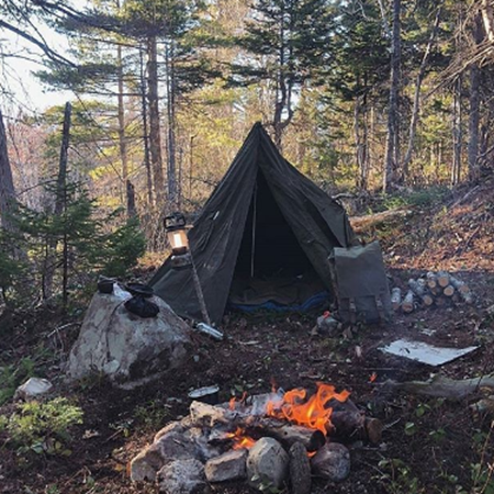 Shows a campsite with tent and campfire in the woods. 