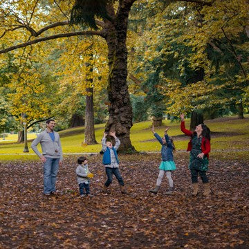 Shows a family playing in the park in autumn with leaves on the ground. 