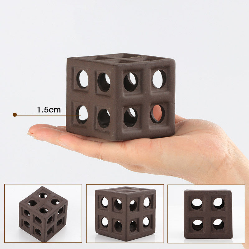 Small brown cube with holes held in a hand, showing its size relative to a finger.