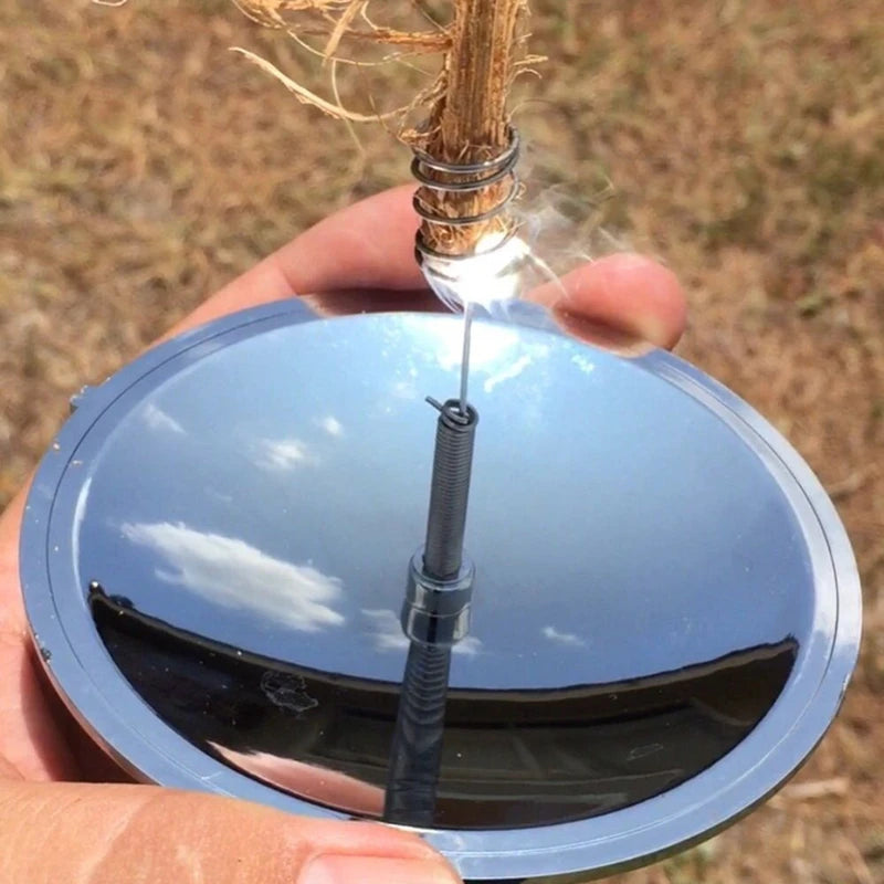Hand holding a reflective solar concentrator with a small flame, against a natural background.