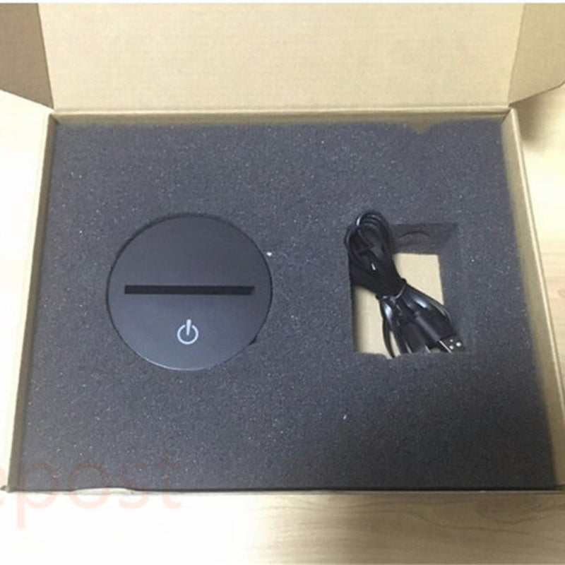 A black circular wireless charging pad with a power symbol, displayed inside its open cardboard packaging with a black foam insert and a black charging cable.