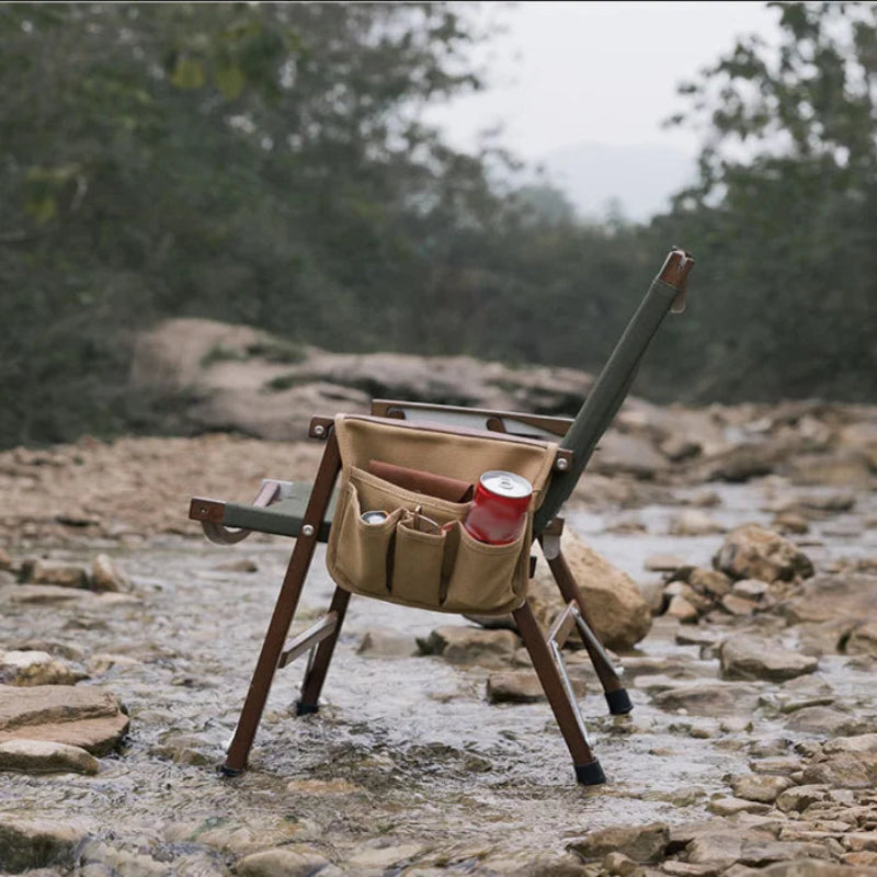 Portable chair with storage pouches and a red can on a rocky riverbank