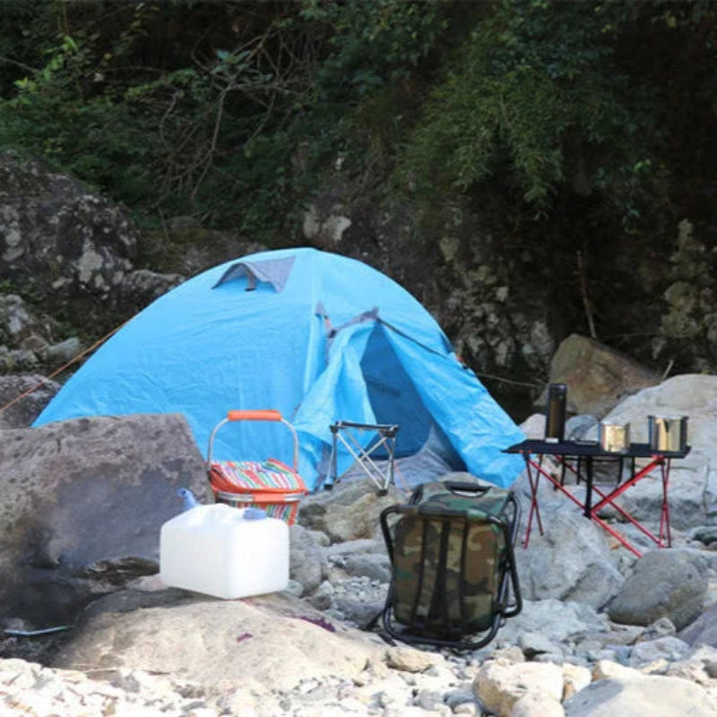 Blue tent set up on a rocky riverbank with camping gear.