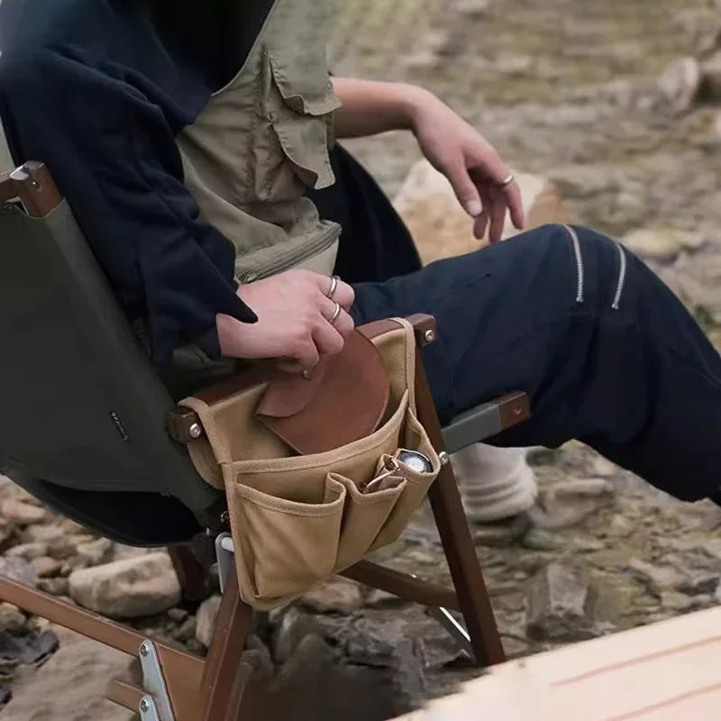 Person sitting outdoors with a beige camping chair pocket holding items