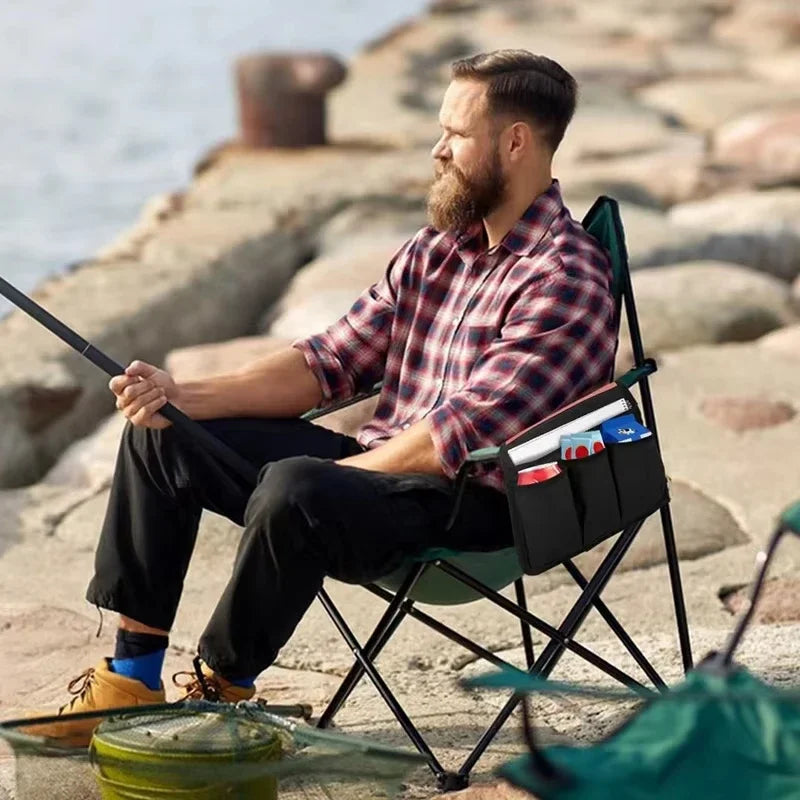 Man sitting on a folding chair by the water, holding a fishing rod.