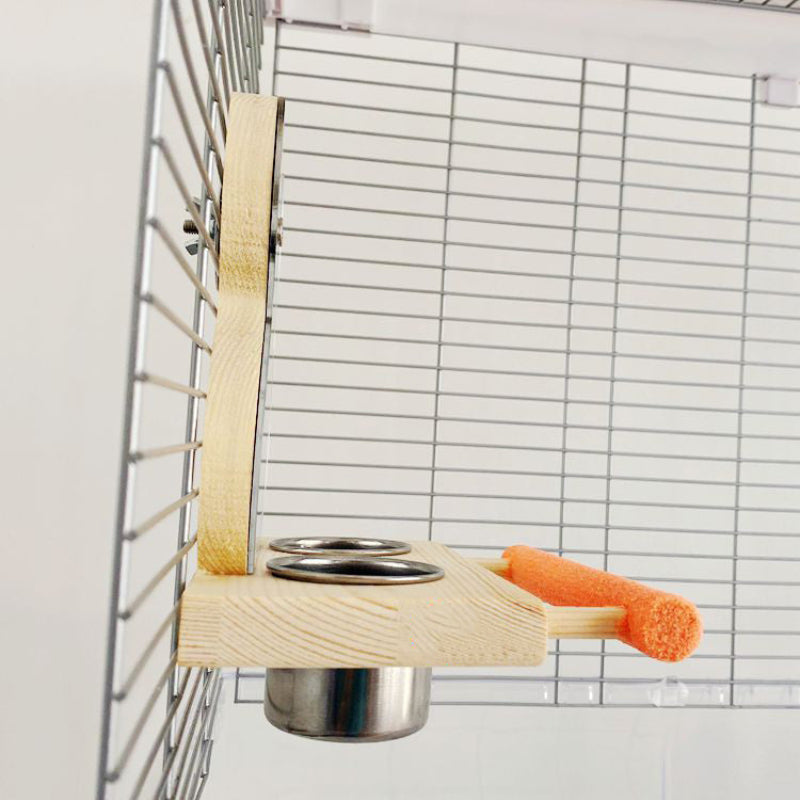 Wooden bird perch with metal cup and carrot attached to a wire cage.