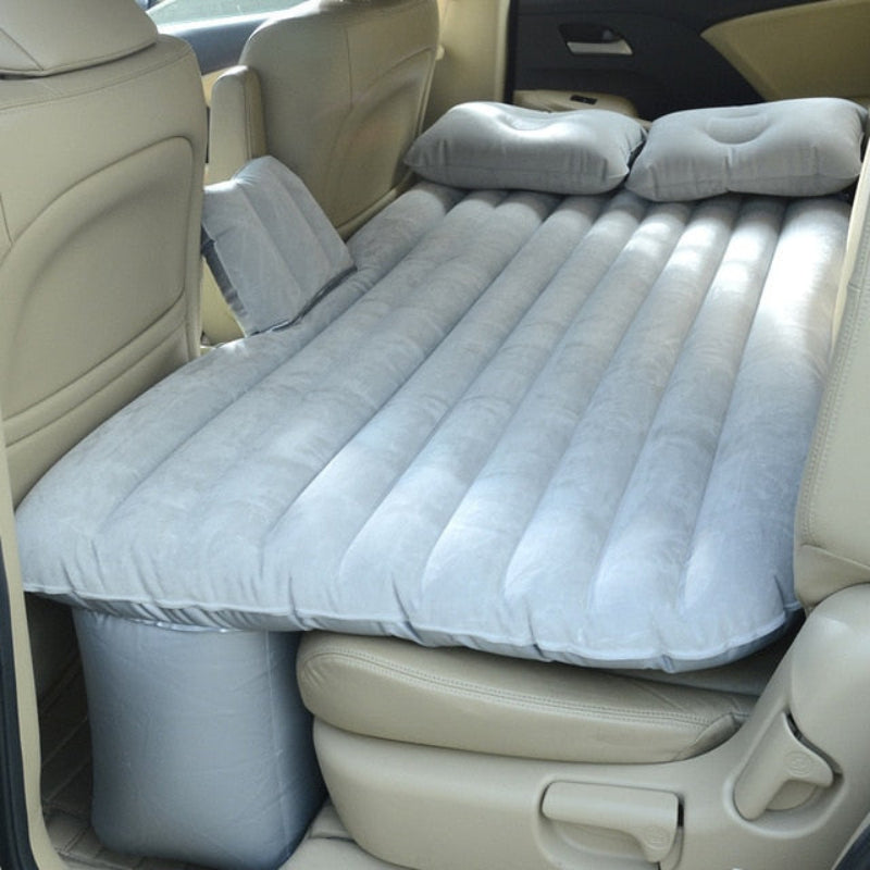 Inflatable mattress set up in the back of a car with pillows.