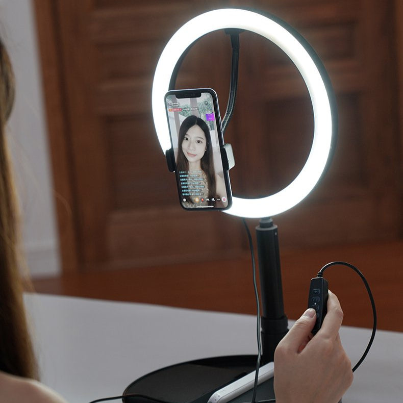 Portable LED ring light with smartphone holder on a wooden floor.