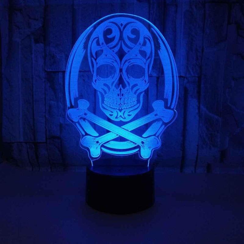 A 3D optical illusion night light featuring a glowing blue skull and crossbones design on a black base, set against a dark textured background.