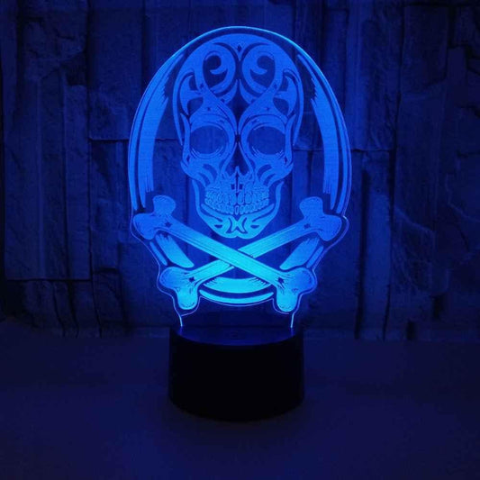 A 3D optical illusion night light featuring a glowing blue skull and crossbones design on a black base, set against a dark textured background.