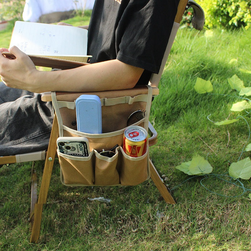 Person sitting outdoors with a chair that has multiple pockets for holding items, including a phone and a can.