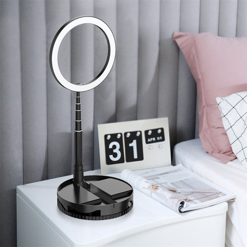 Black desk lamp with round mirror on a nightstand next to a calendar and newspaper.