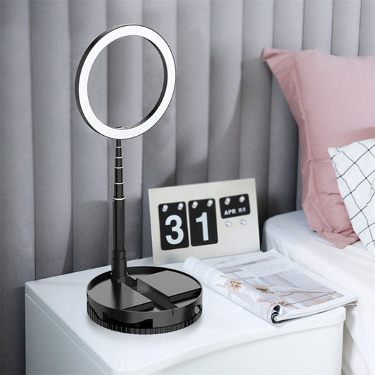 Black desk lamp with round mirror on a nightstand next to a calendar and newspaper.
