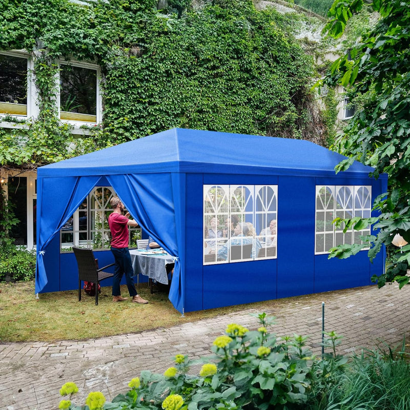 Blue outdoor canopy tent set up in a garden with people inside, surrounded by greenery.