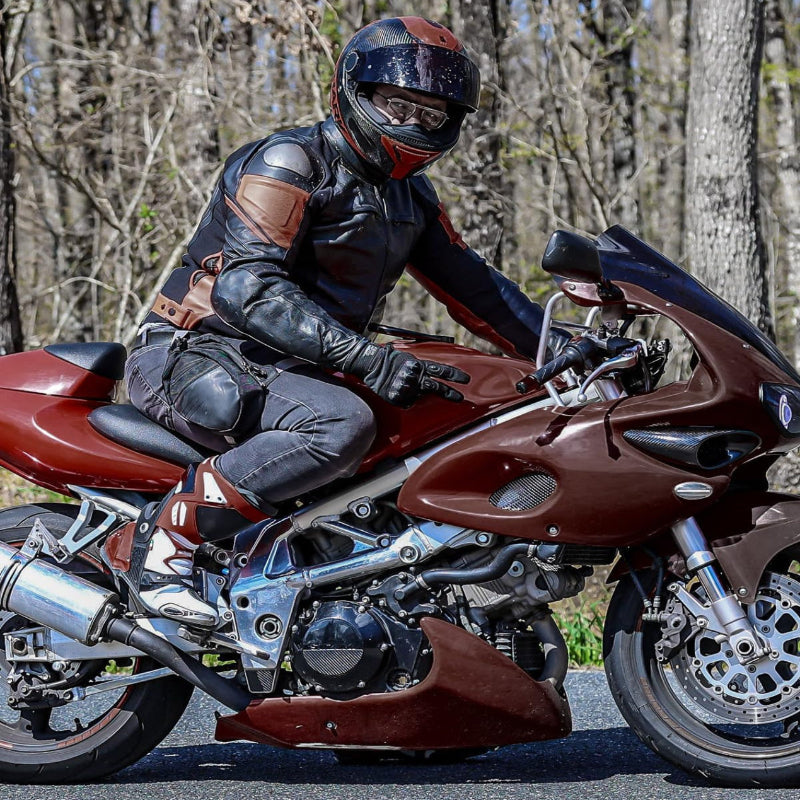 Person riding a red motorcycle on a road with trees in the background