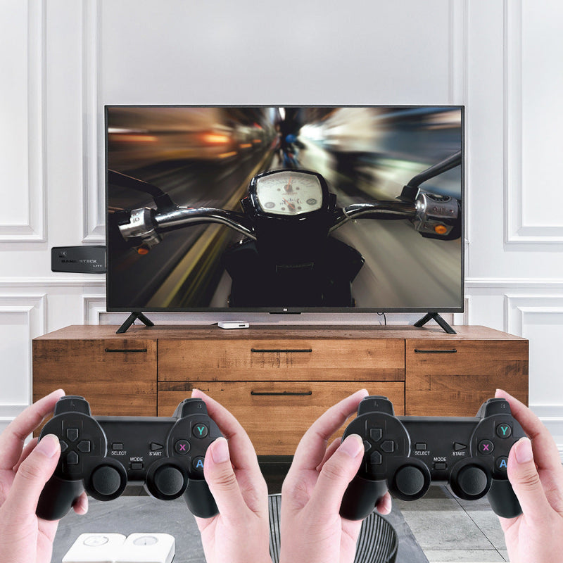 Two hands holding gaming controllers in front of a TV displaying a motorcycle game.