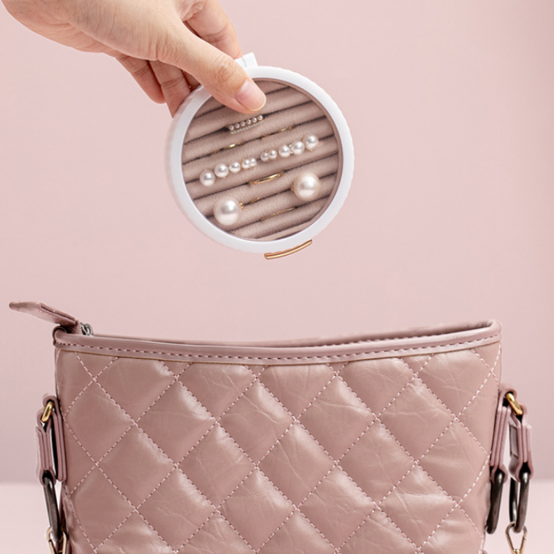 Pink quilted handbag with a round jewelry case containing pearls on a pink background