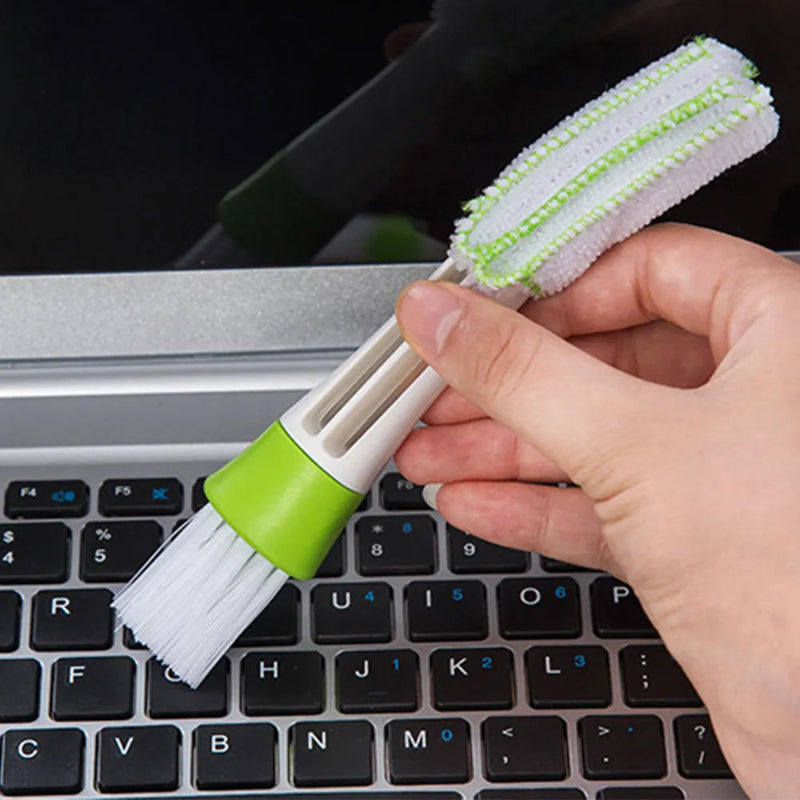 Cleaning brush with green handle held over a laptop keyboard