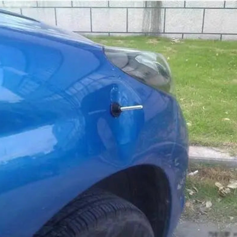 Blue car with a small object attached to its side, on a grassy area.