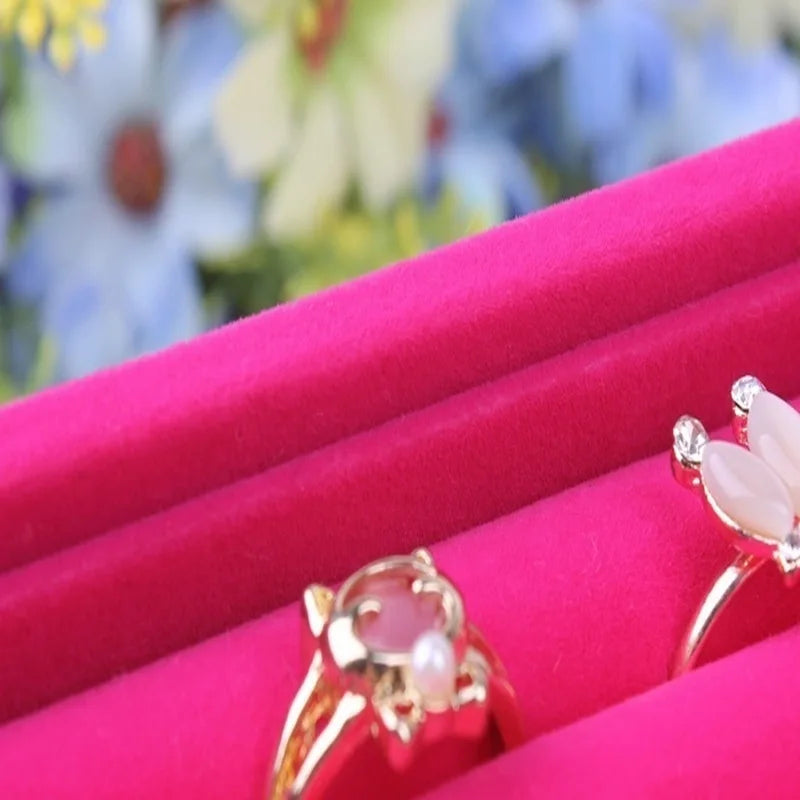 Gold rings with gemstones on a pink cushion with a blurred floral background