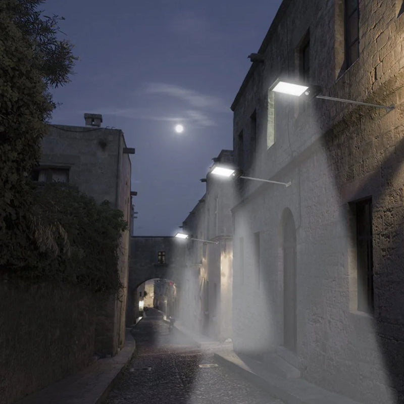 Street scene at night with illuminated streetlights casting shadows on stone buildings.