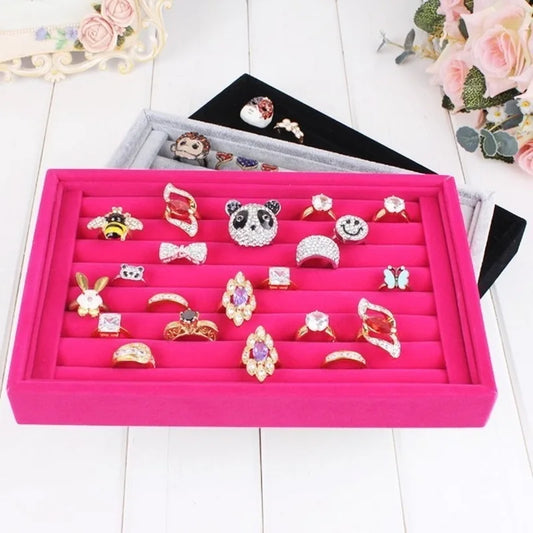 Pink jewelry display tray with various rings on a white surface.
