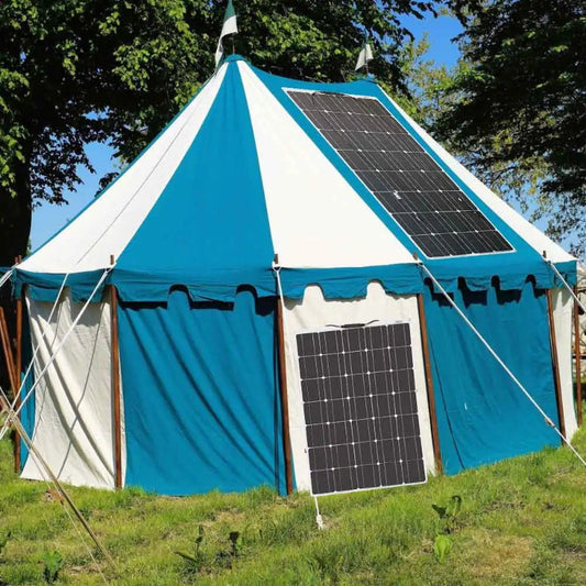 Blue and white tent with solar panels on a grassy area with trees in the background