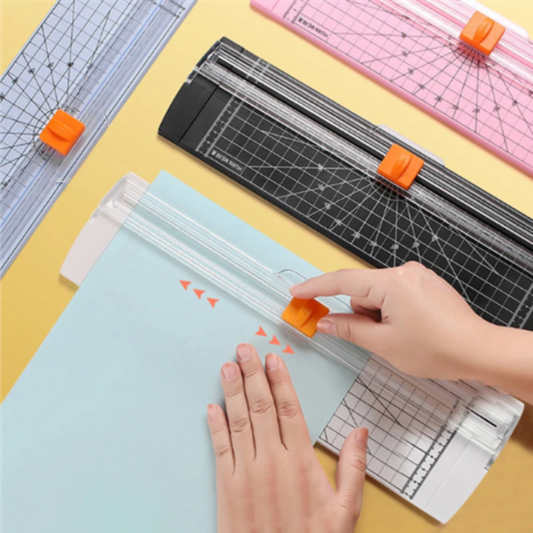 Person using a paper cutter on a yellow surface with multiple cutters visible