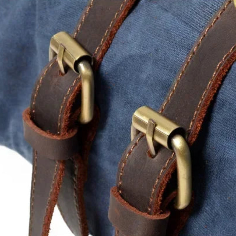 Close-up of a blue bag with brown leather straps and brass buckles.