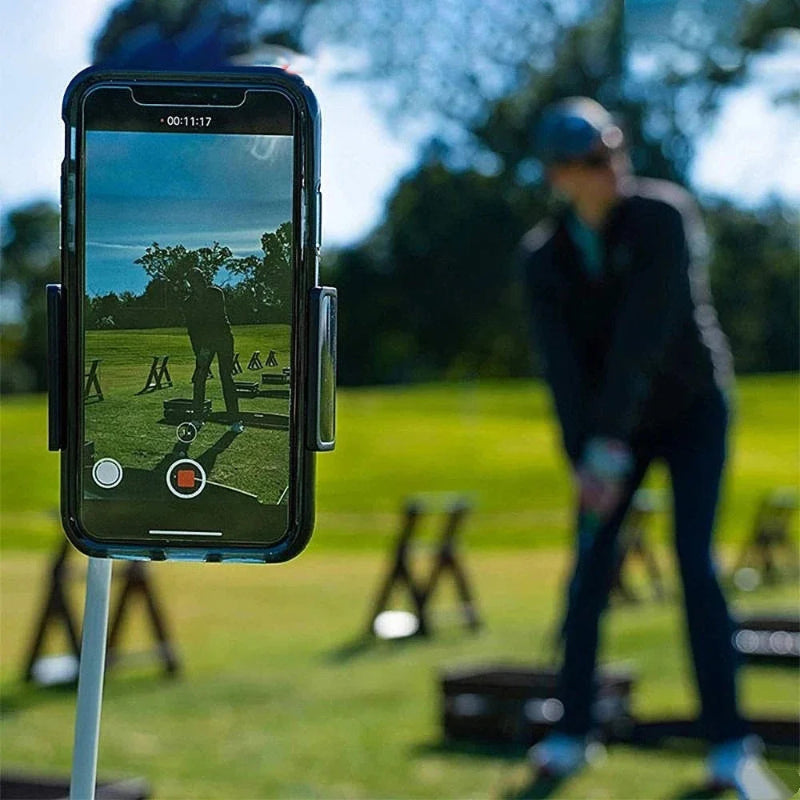 Person taking a photo of another person playing golf with a smartphone on a stand.