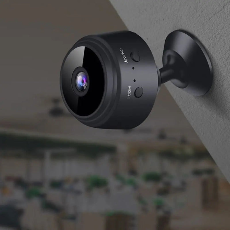 Black security camera mounted on a wall with a blurred indoor background