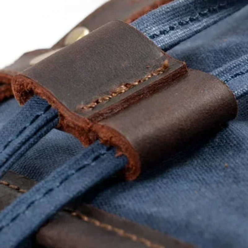 Close-up of a blue denim bag with brown leather straps and stitching.