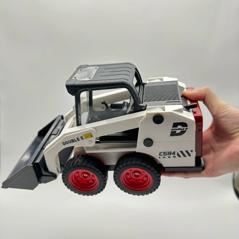 A miniature toy double-ear skid steer loader held in a person's hand against a plain light gray background. The toy is primarily white with a black cabin and bucket, and features red wheels.