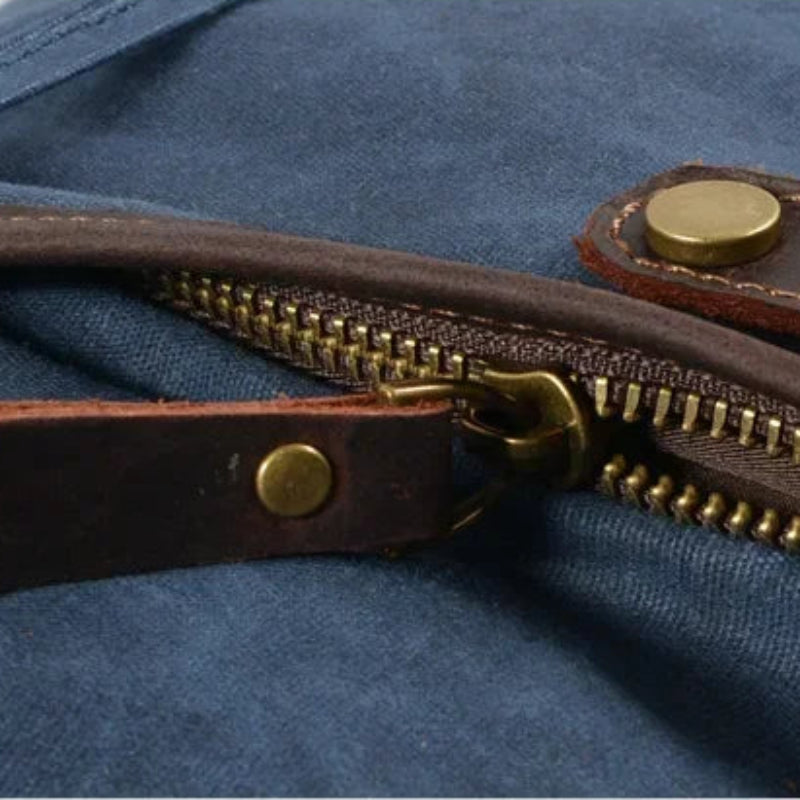 Close-up of a blue bag with a brown leather zipper and gold metal pull.