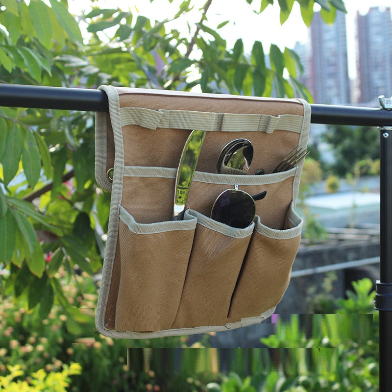 Beige tool pouch with multiple pockets hanging on a railing with a cityscape in the background
