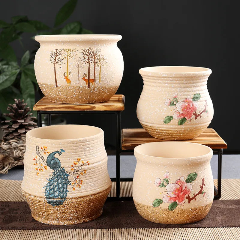 Four hand-painted ceramic planter pots in a warm beige speckled glaze, displayed on small wooden risers against a dark background. The pots feature various nature illustrations, including a blue peacock, a tree with deer, and pink floral designs.