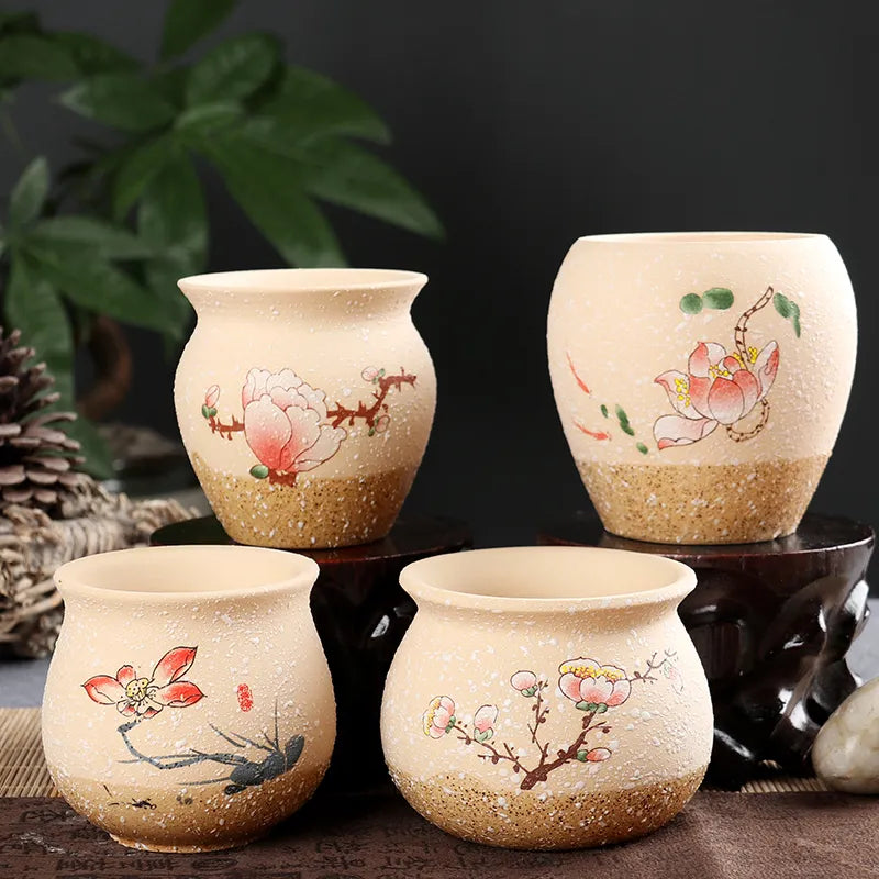 Four hand-painted ceramic tea cups with floral designs, arranged on dark wooden stands against a dark background with a green plant leaf in the upper left.