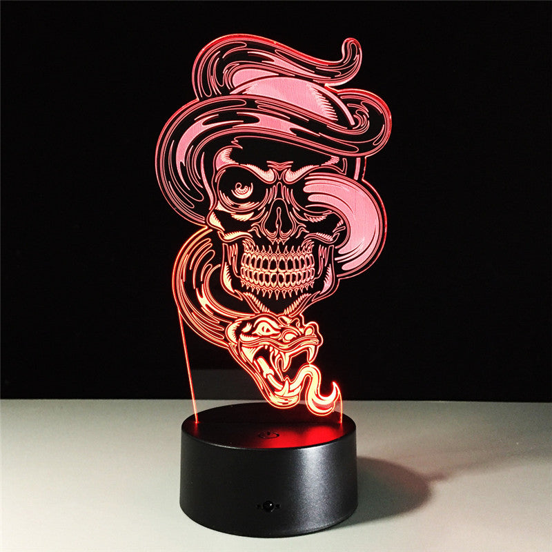 An LED 3D optical illusion lamp featuring a stylized skull wearing a hat and smoking a cigar, glowing with red and pink light on a black cylindrical base.