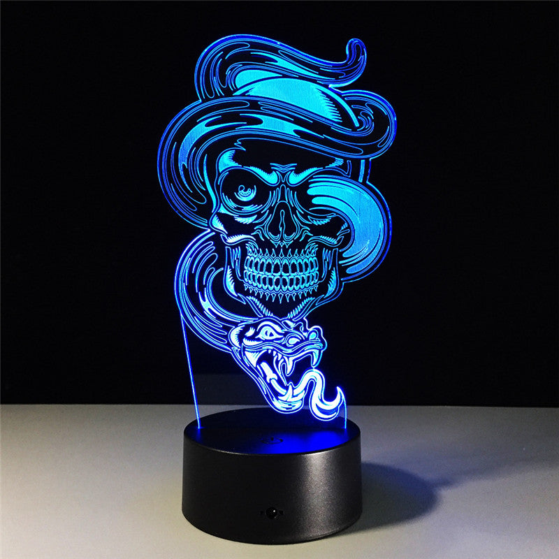 A 3D optical illusion LED night light featuring a glowing blue skull wearing a hat and a snake, mounted on a black cylindrical base against a dark background.